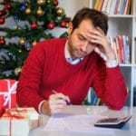 man uses pen and calculator gifts and tree in background