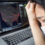 woman with mask on looks at covid map and cries
