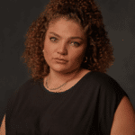 A curly haired woman wearing a black dress as she poses for a picture.